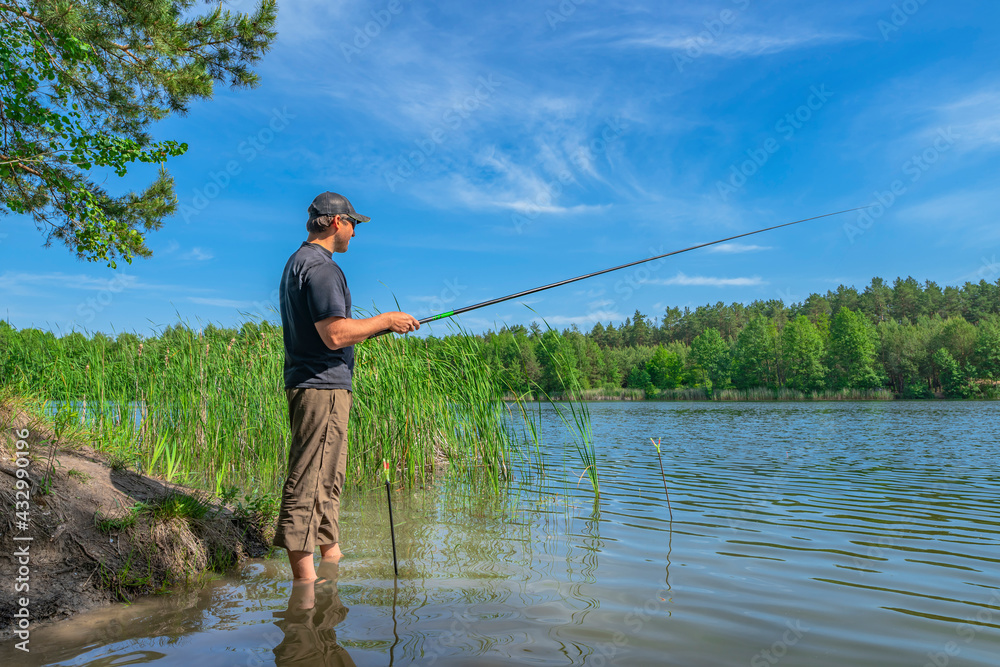Fishing. Angler with float pole rod catch fish on on beautiful lake at green forest. Fisherman in action, man stand in water Fishing. Angler with float pole rod catch fish on on beautiful lake at green forest. Fisherman in action, man stand in water