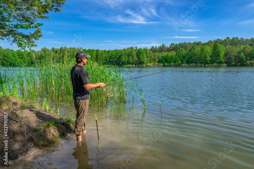 Fishing. Angler with float pole rod catch fish on on beautiful lake at green forest. Fisherman in action, man stand in water