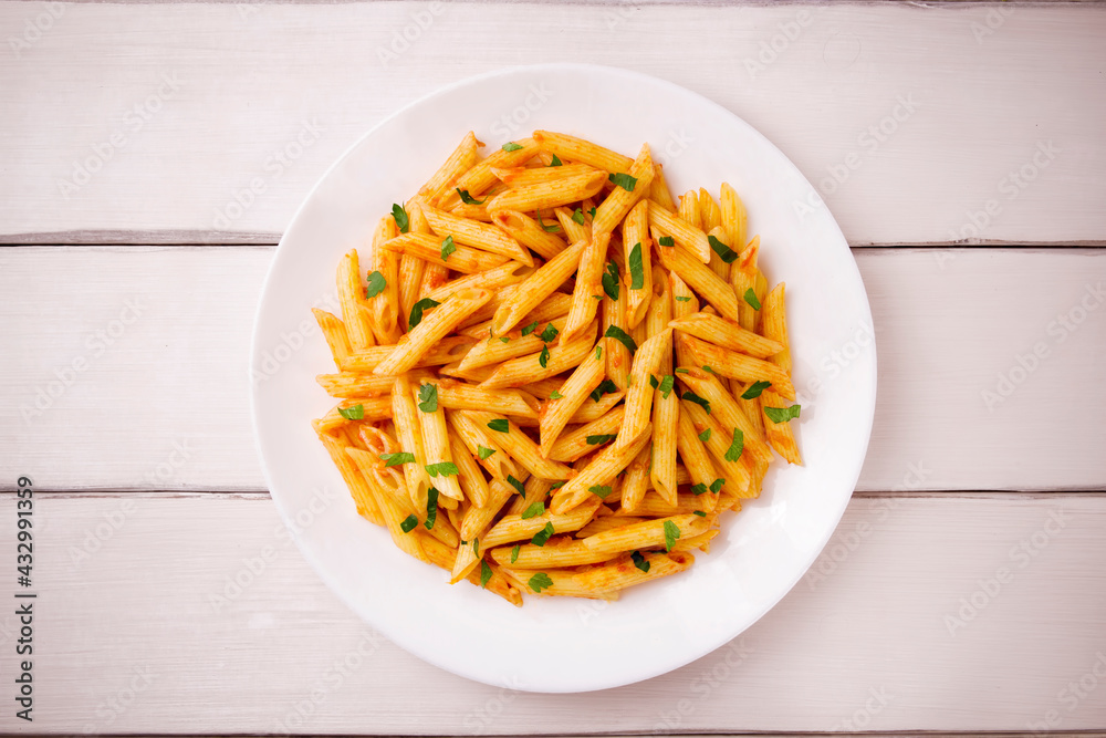 Penne pasta in tomato sauce, decorated with parsley on a white wooden table Penne pasta in tomato sauce, decorated with parsley on a white wooden table