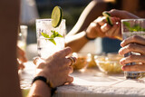 Hands holding a fresh alcoholic long drink cocktail on a table. Gathering of friends in an outdoor pub in the summer.