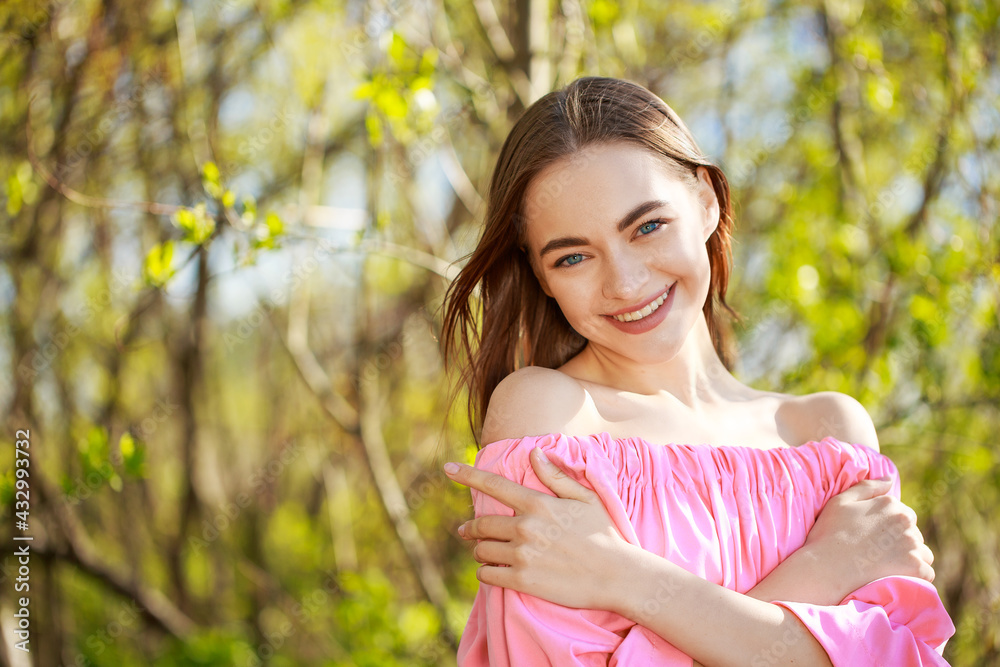 Portrait of a beautiful young woman of European appearance in a pink dress on a natural background smiling, face skin care concept Portrait of a beautiful young woman of European appearance in a pink dress on a natural background smiling, face skin care concept