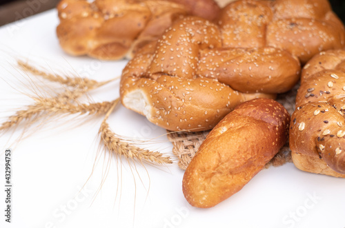 Fresh crispy bread  with spikelets of wheat on wicker napkin and white background table. Harvest season holiday World Bread Day. Bread is the staff of life. Side view. Close-up.