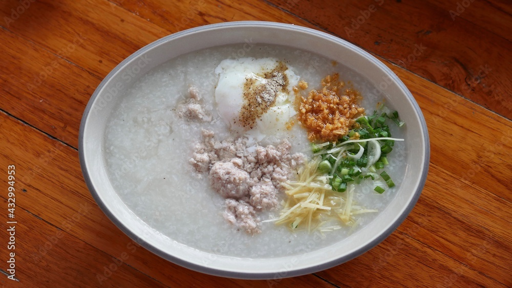 Asian congee with ground pork, egg and vegetable in a bowl on wooden background. Asian congee with ground pork, egg and vegetable in a bowl on wooden background.