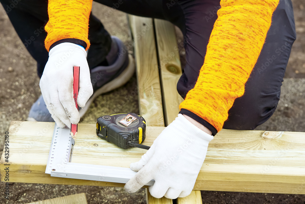diy Carpenter marks a piece of wood. carpenter's hands in white gloves, pencil, tape measure and square - a tool for precise work. Carpenter applying marking onto wooden board