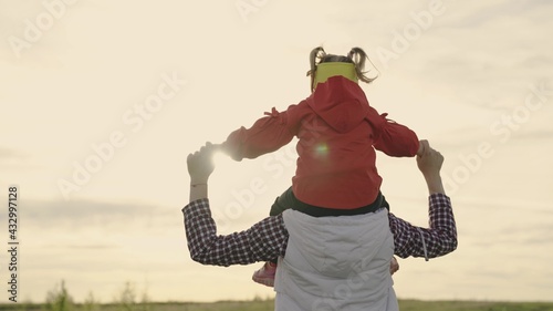 Mom plays with her daughter in spring and carries her beloved child on her shoulders in sun. Happy family in park. Mother walks with baby on her shoulders in rays of sunset. Child and parent together