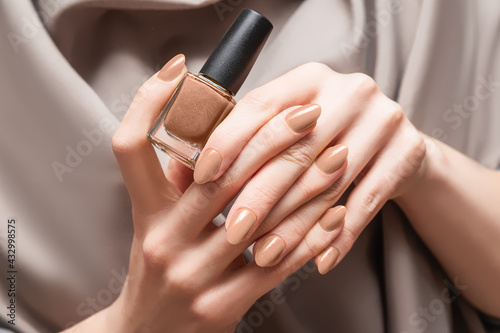 Female hand with beige nail design. Brown nail polish manicure. Woman hand hold beige nail polish bottle.