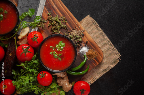 Close-up of Indian Homemade fresh and healthy tomato soup garnished with fresh coriander leaves and ingredients and herbs, served in a black bowl over the wooden top background. 