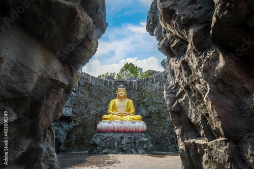 The gold Buddha statue with waterfall and stone wall in the background at Wat Lak Si Rat Samoson, Samut Sakhon, Thailand photo