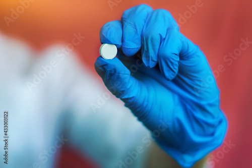 A young nurse, a doctor in latex blue gloves, holds a single white pill in her hand. Close-up of medical pills in the doctor's hand for medical care design. The concept of medical care, protection