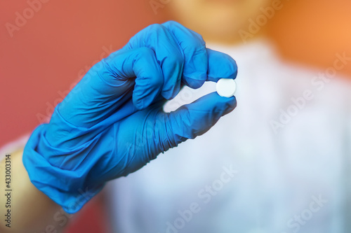 A young nurse, a doctor in blue rubber gloves, holds a white pill between her fingers. Close-up of an antibiotic in the hand for treatment. The concept of medical care, protection, rescue
