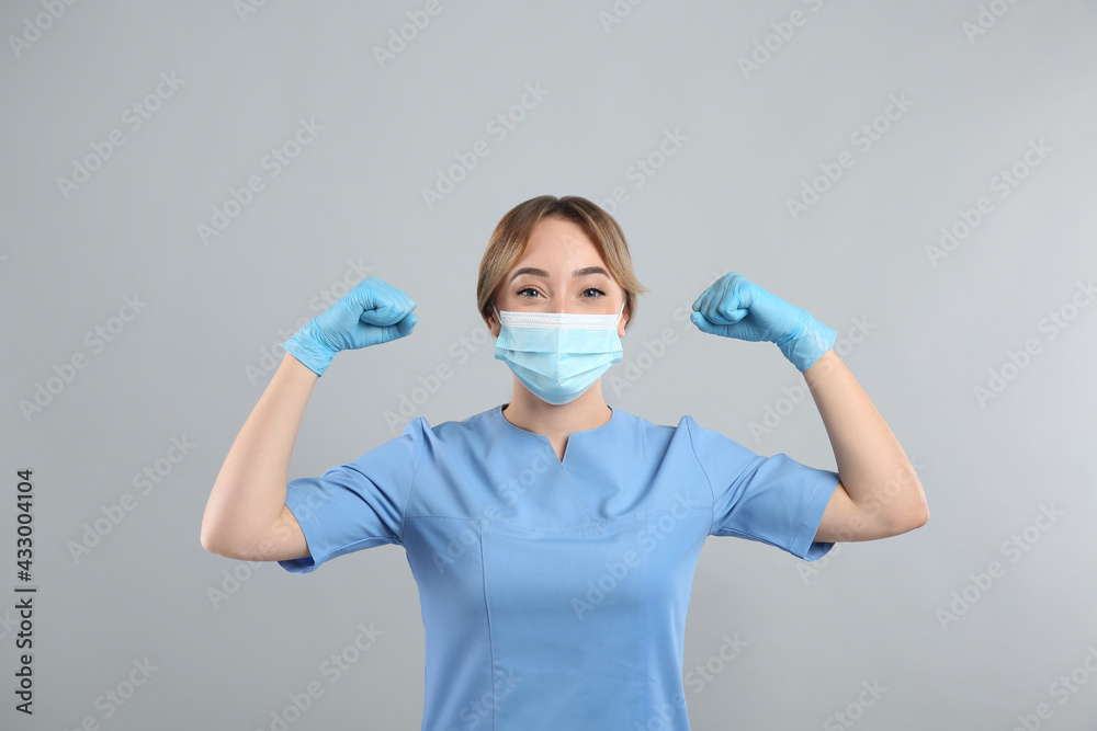 Doctor with protective mask showing muscles on light grey background. Strong immunity concept