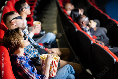 Friends are watching a movie in the cinema. People sit in the armchairs of the cinema and look at the screen with special glasses for 3D