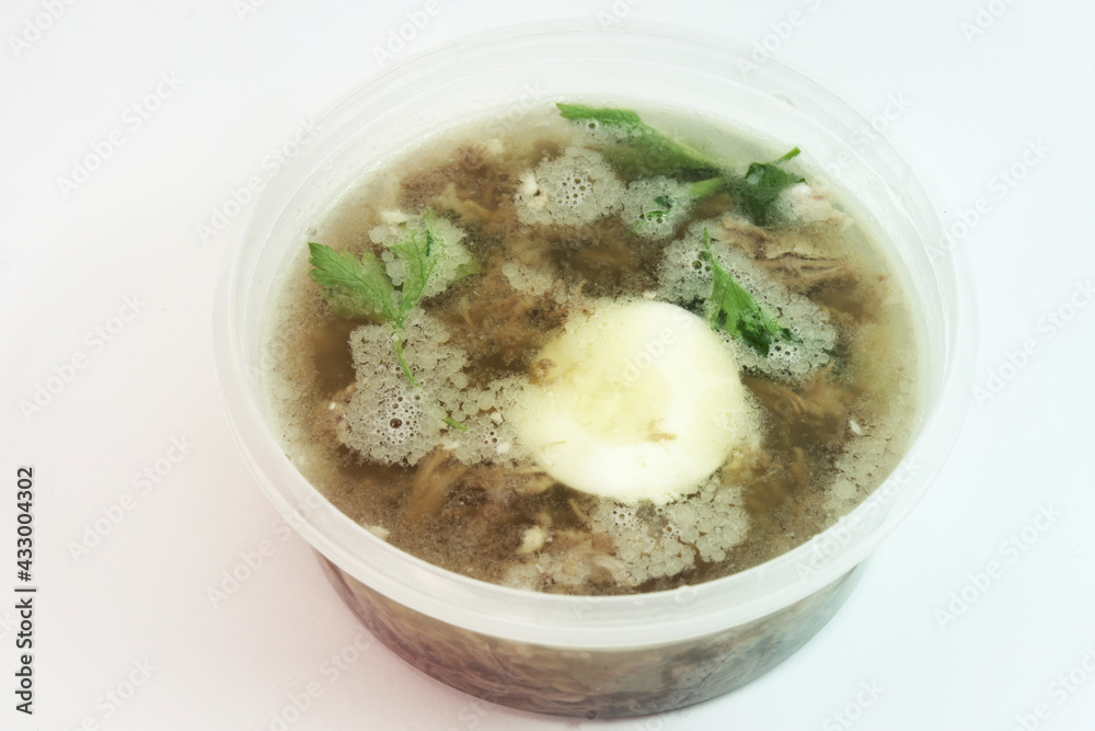 aspic with meat, eggs and fresh parsley, made with thick and rich nutritious bone broth, frozen in round transparent plastic food container