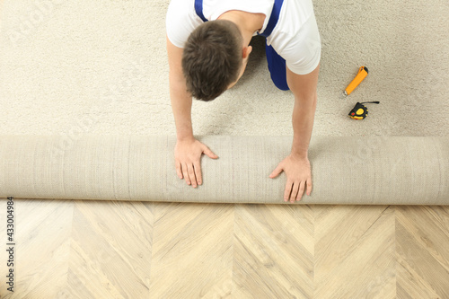Fotografie Worker rolling out new carpet flooring indoors, top view
