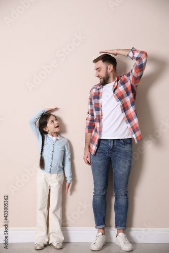 Father and daughter comparing their heights near beige wall indoors