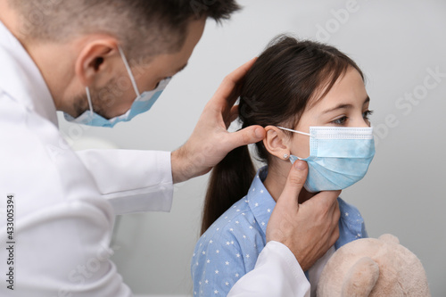 Pediatrician examining little girl in hospital. Doctor and patient wearing protective masks