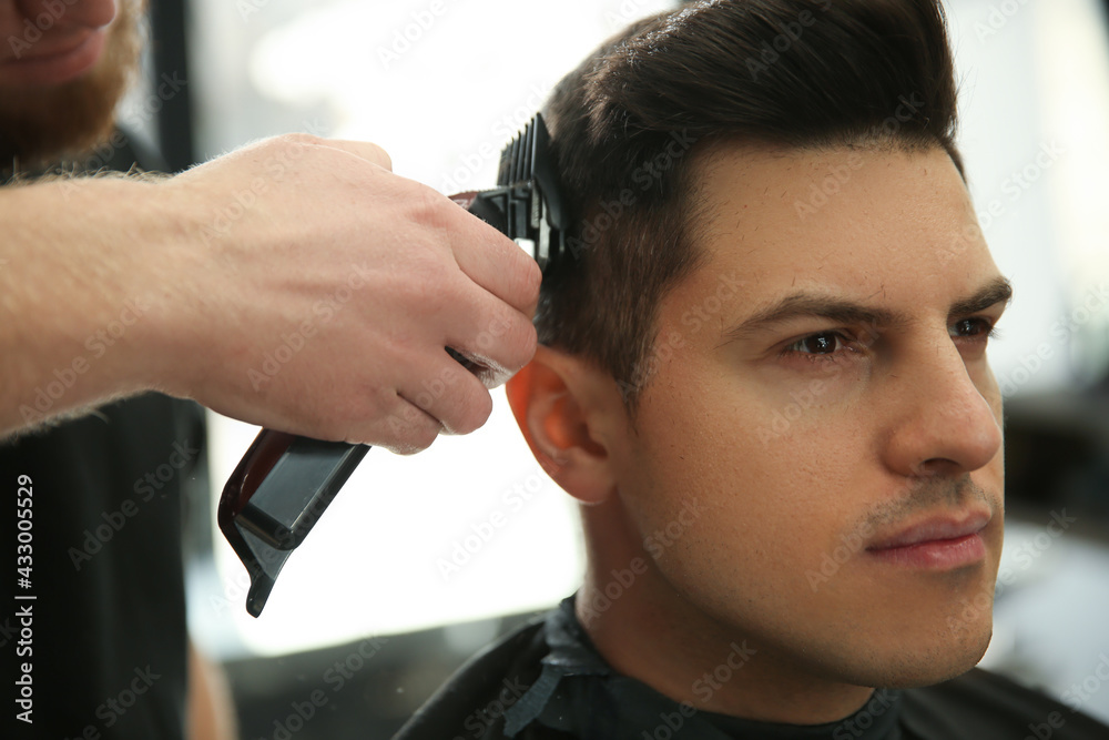 Professional barber making stylish haircut in salon, closeup