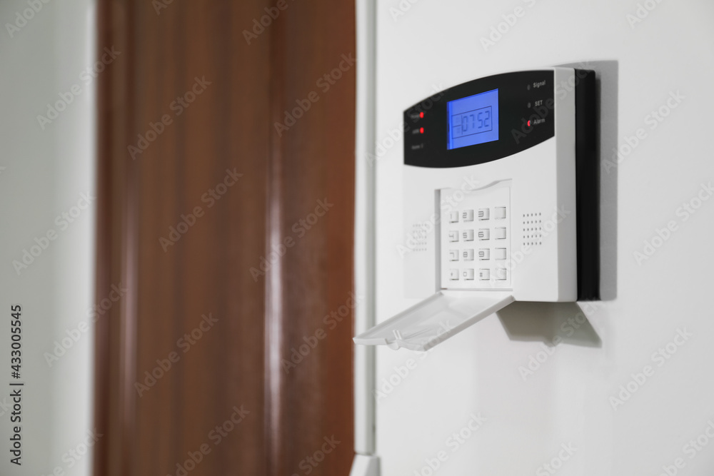 Home security alarm system on white wall near door, space for text Home security alarm system on white wall near door, space for text