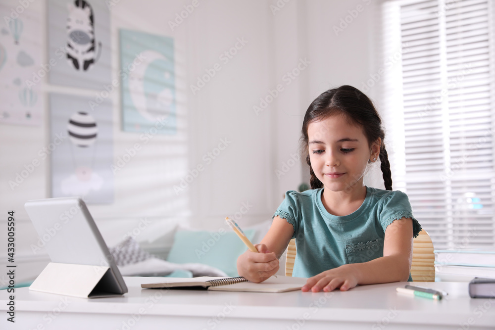 Little girl doing homework with tablet at table in room Little girl doing homework with tablet at table in room