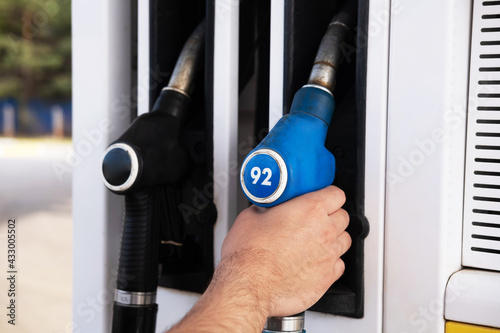 Refueling the car with fuel. There are black and blue pistols on the gas pump for refueling the car with gasoline. The man takes the blue pump.