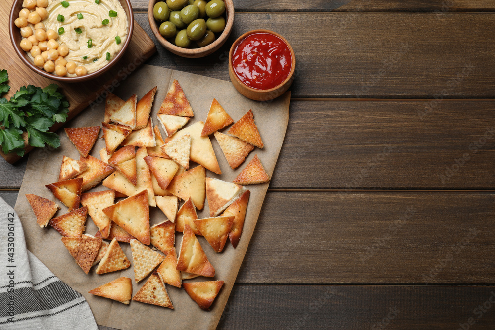 Delicious pita chips with hummus, olives and sauce on wooden table, flat lay. Space for text