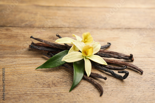 Beautiful vanilla flowers and sticks on wooden table, closeup