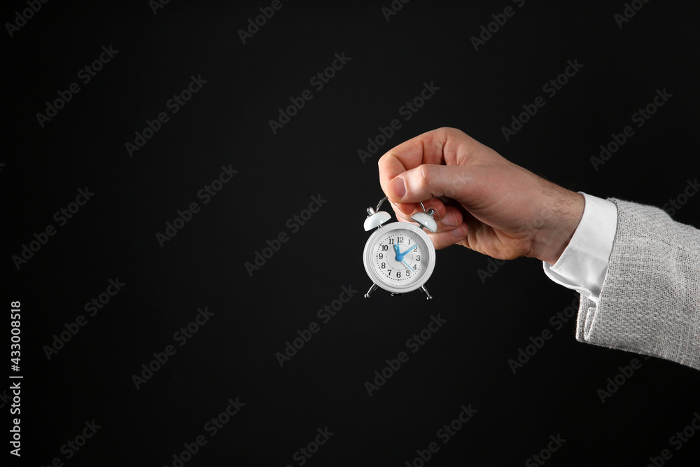 Closeup view of businessman holding tiny alarm clock on black background, space for text. Time management