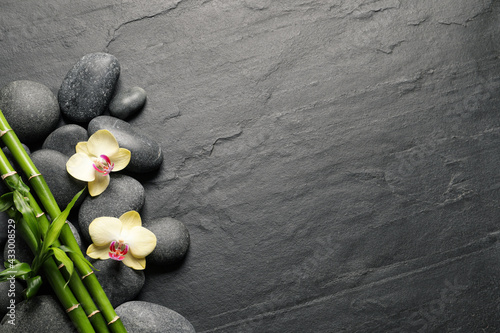 Spa stones, beautiful orchid flowers and bamboo stems on black table, flat lay. Space for text photo