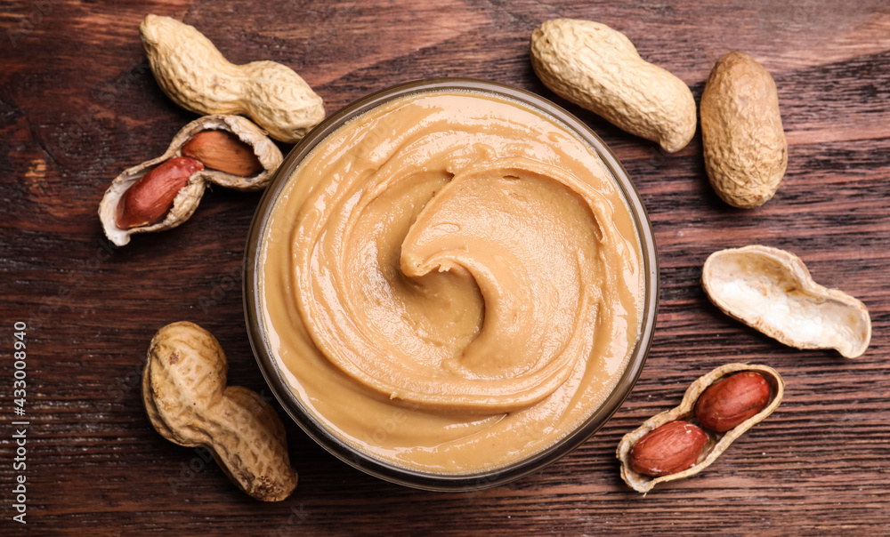 Fototapeta premium Yummy peanut butter in glass bowl on wooden table, flat lay