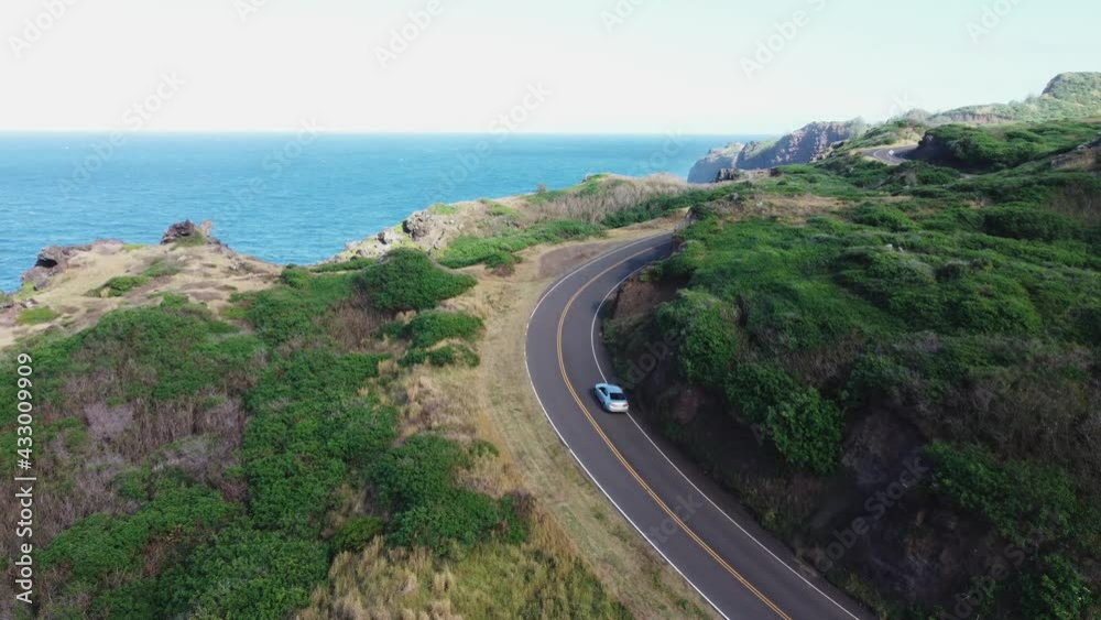 Aerial tracking shot of car driving curve on rural ocean road with overgrown cliffs and rocks during sunny day. Slow motion shot. Aerial tracking shot of car driving curve on rural ocean road with overgrown cliffs and rocks during sunny day. Slow motion shot.