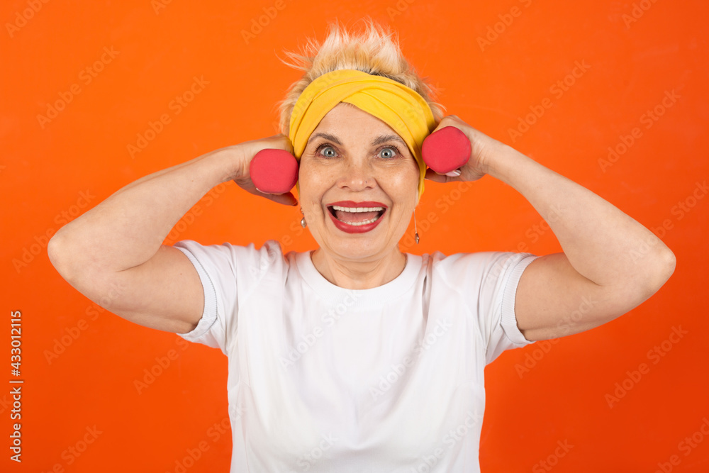 adult woman pensioner goes in for sports with dumbbells on orange background adult woman pensioner goes in for sports with dumbbells on orange background