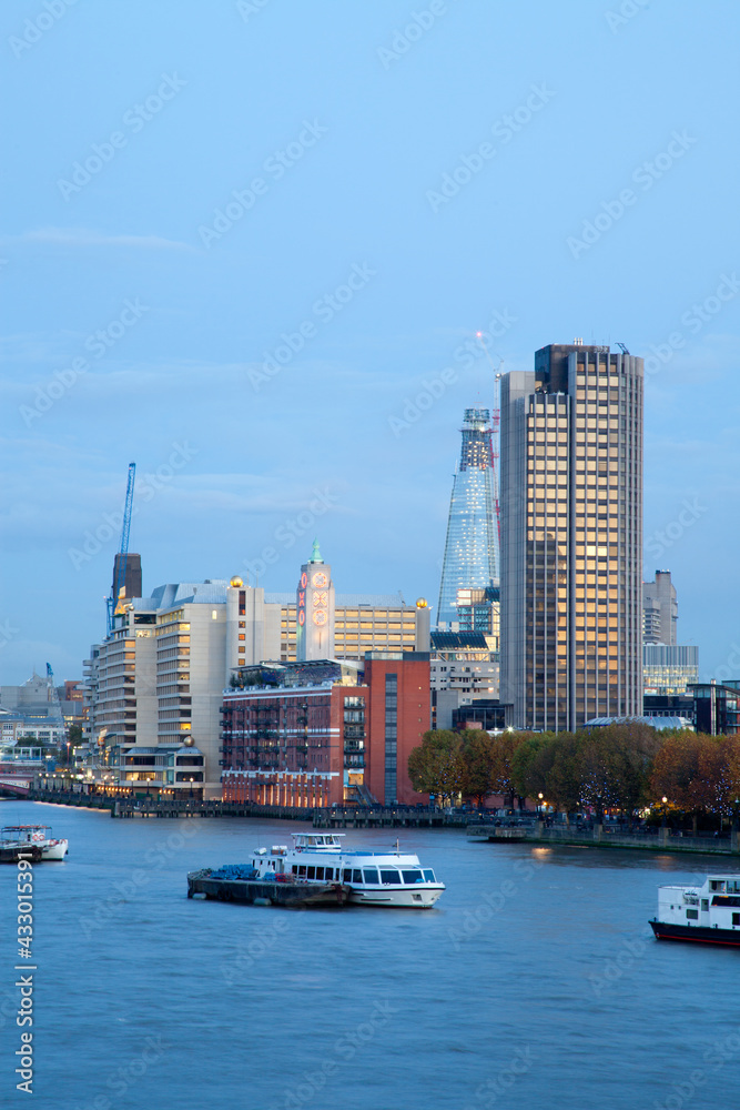 Fototapeta premium Vertical crop portrait of the River Thames in London at evening showing boats in the foreground and the oxo building and partially built shard 