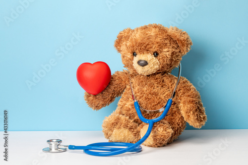 Children's doctor or family doctor. Teddy bear with a stethoscope is holding red heart