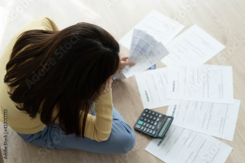 Women stress about a lot of credit card debt and bills on the floor. The housewife has trouble calculating monthly expenses and the budget is not enough to pay off the debt