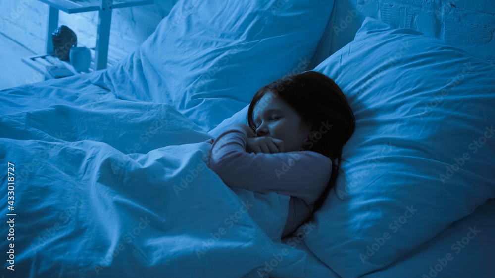 Preteen kid hugging blanket while sleeping on bed Stock Photo