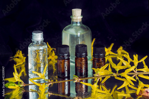 An assortment of cosmetic, pharmaceutic flasks together with yellow flowers placed on reflectig surface and covered with water drops. Pharmaceutic and cosmetic implements concept. photo