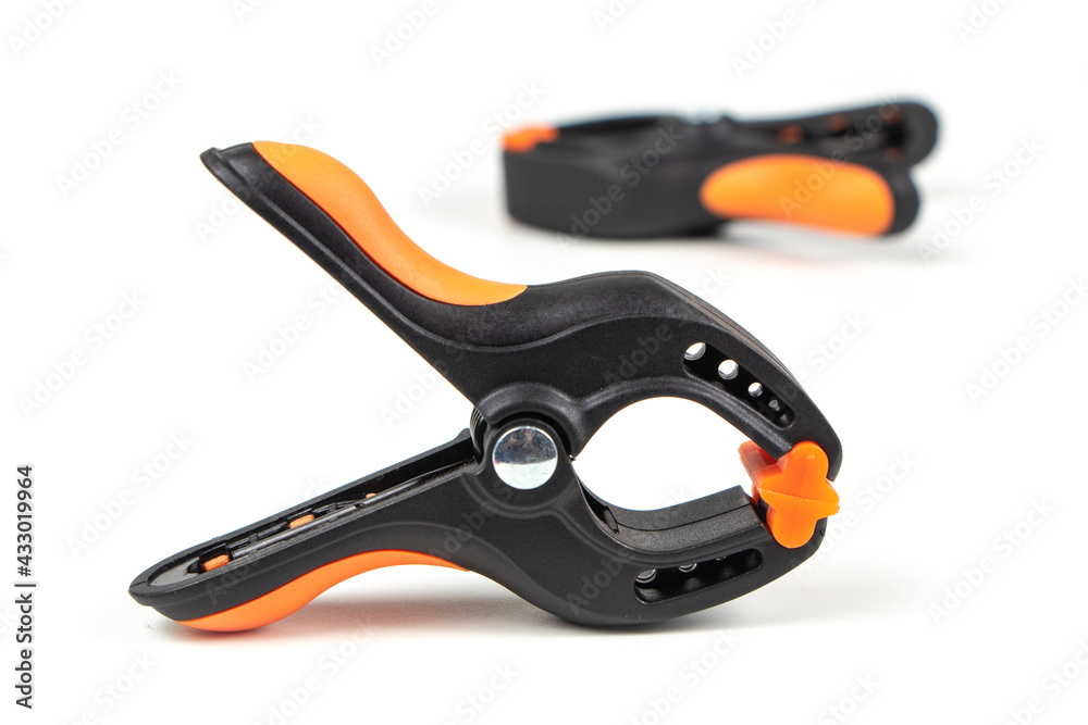 Plastic spring clamp isolated on white background. Clamping equipment. Working hand tool. Black and orange spring clamp. Closeup.. Plastic spring clamp isolated on white background. Clamping equipment. Working hand tool. Black and orange spring clamp. Closeup..
