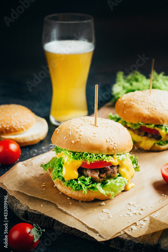 close-up of a hamburger with meat on a grill tomato and greens on the background of a glass with beer on a black background