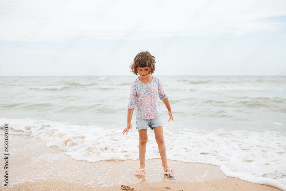 Five years cute curly caucasian girl painting on sand on the beach.