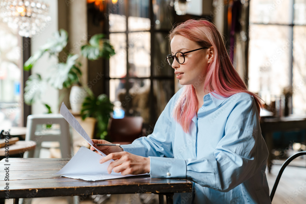 Young beautiful woman with pink hair doing paperwork in cafe