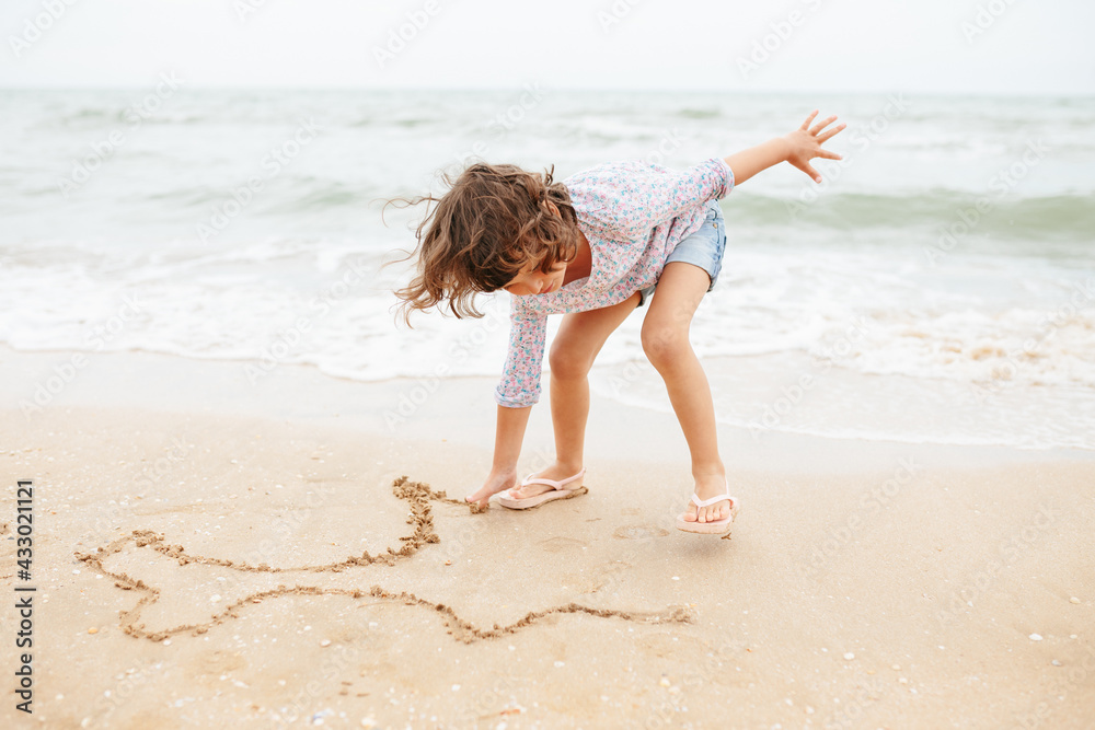 Five years cute curly caucasian girl painting on sand on the beach. Five years cute curly caucasian girl painting on sand on the beach.