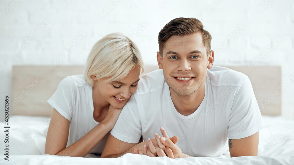joyful man and cheerful woman holding hands on bed joyful man and cheerful woman holding hands on bed