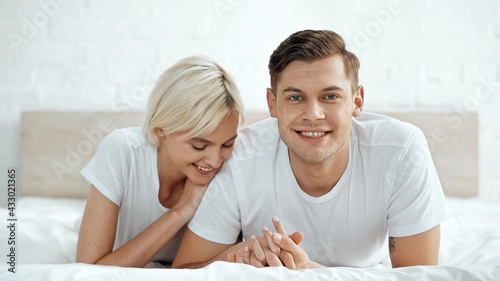 joyful man and cheerful woman holding hands on bed