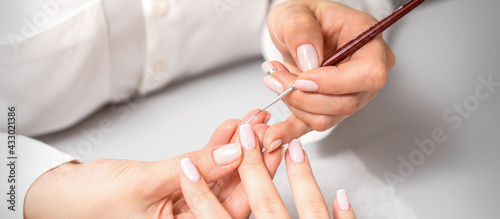 French manicure. Manicure master drawing white varnish on the nail tip with a thin brush  close up