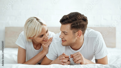 cheerful man holding hands with cheerful woman on bed