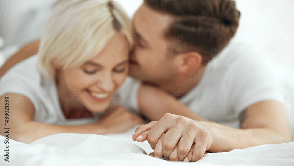 blurred young woman and man holding hands and smiling in bed