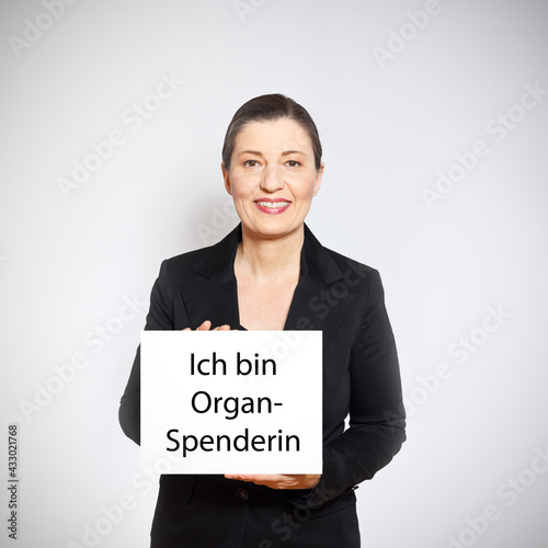 Organ donation concept: mature woman holding up a white sign with the text I am an organ donor in german. photo