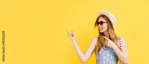 Young surprised woman, in a summer hat, pointing and looking to the left at a logo, showing an advertisement, on a yellow background.
