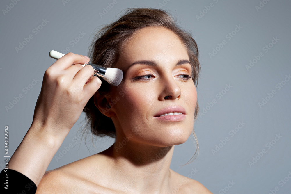 Fototapeta premium Applying natural makeup on a beautiful woman. Applying powder with a wide brush
