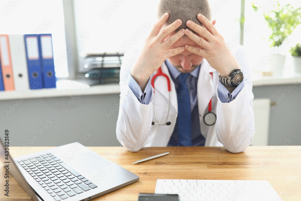 Tired doctor sitting at table and holding his head Tired doctor sitting at table and holding his head